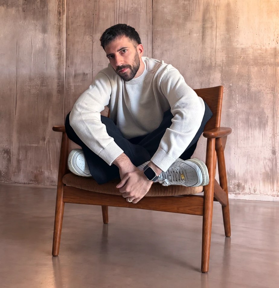 Marco Cassano sitting cross-legged on a wooden armchair